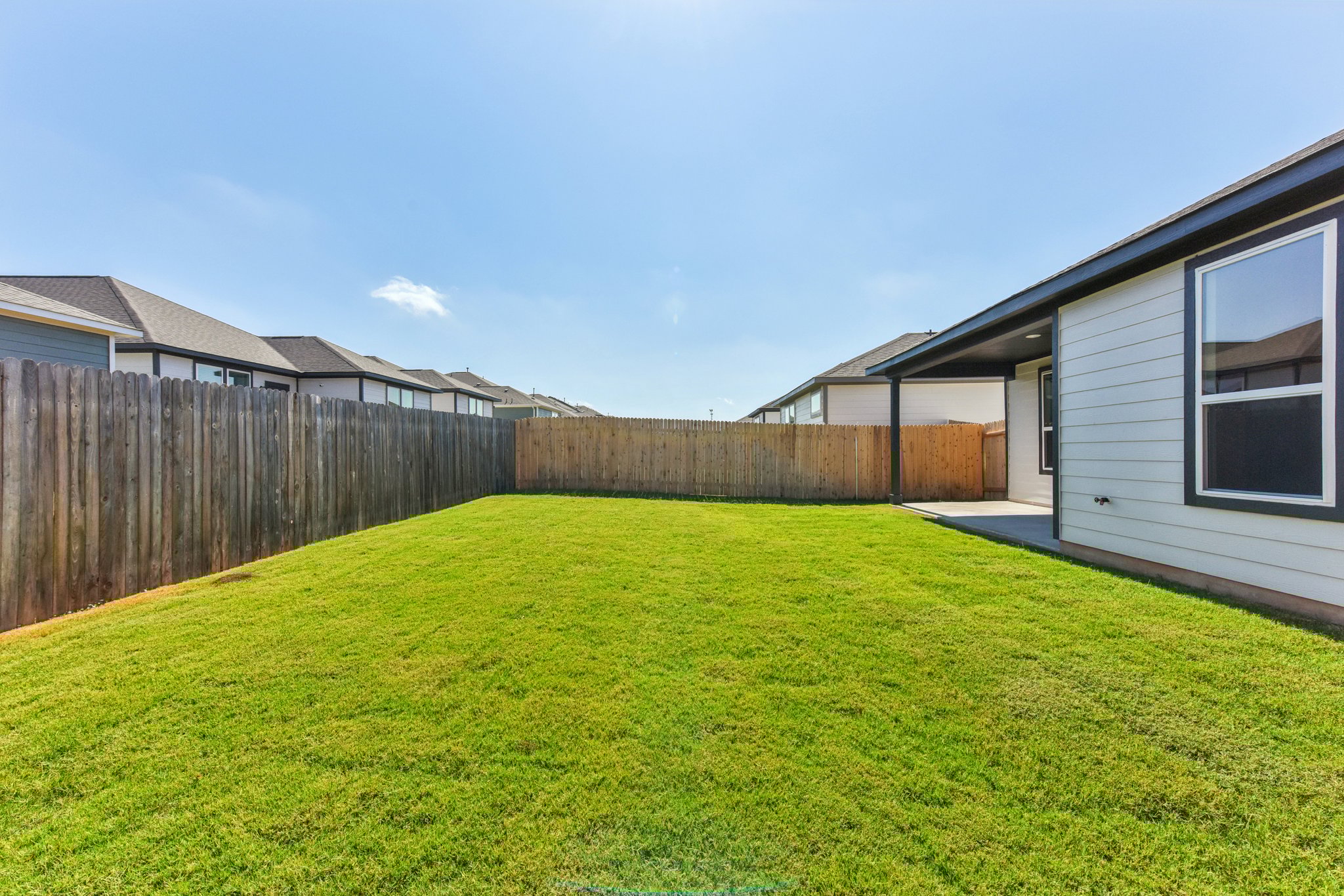 A fenced in yard with a house and a grass yard.