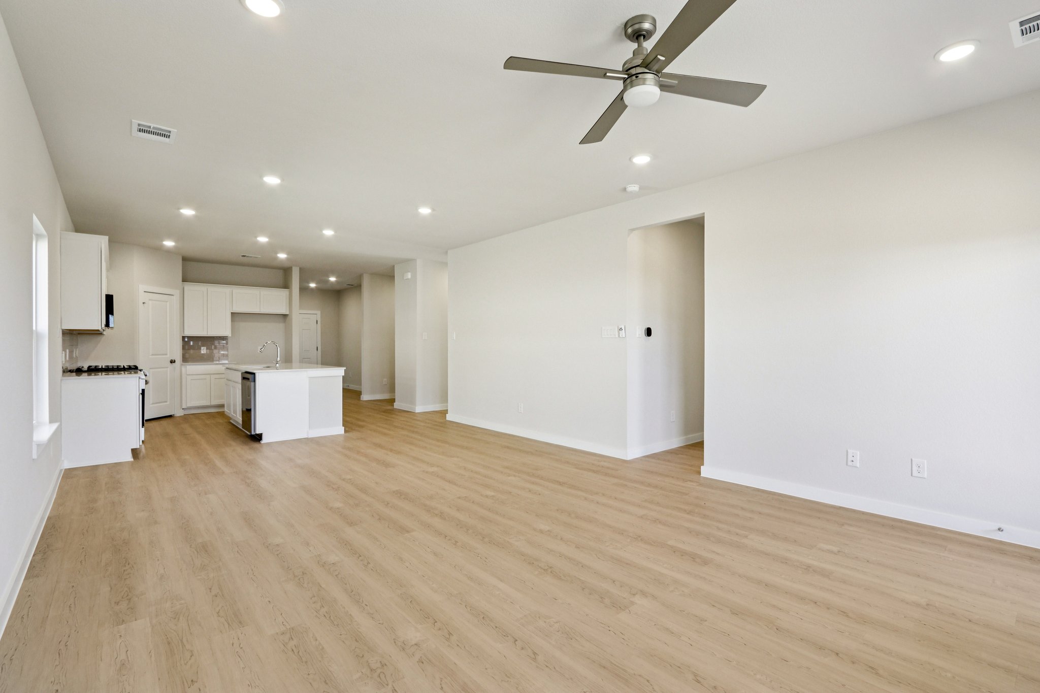 A large empty room with a ceiling fan and a wood floor.
