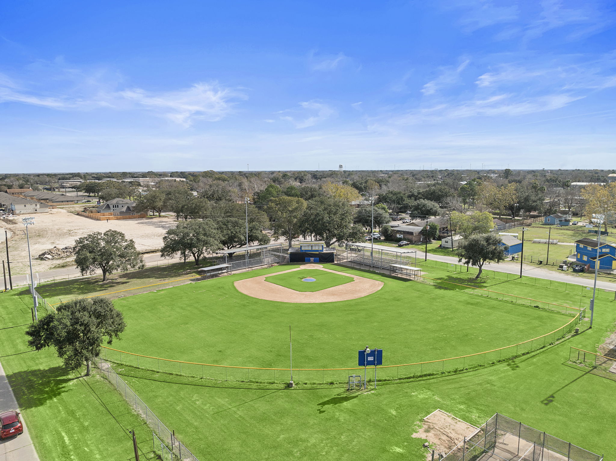 A large green field with a few trees and a few buildings.