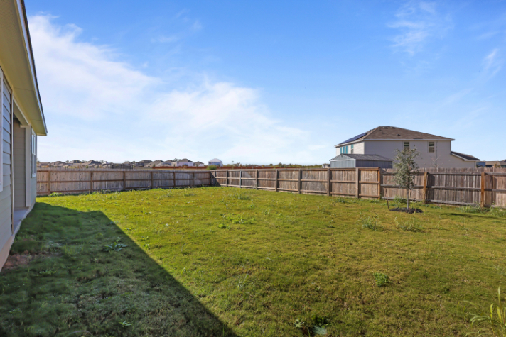 A fenced in yard with a house and trees in the background.